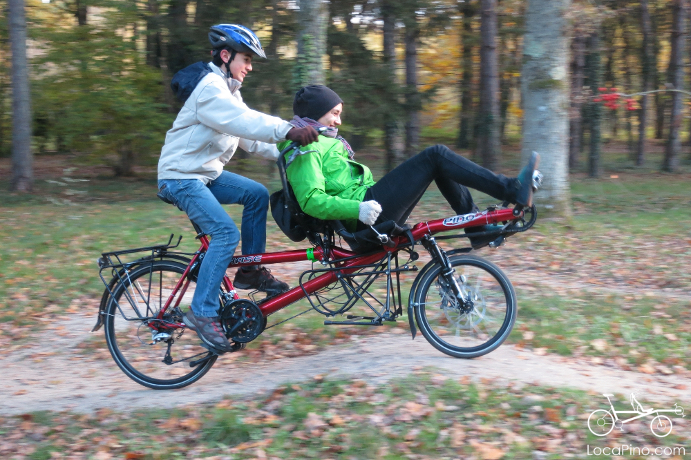 Two people playing with a Pino semi recumbent tandem bike in a forest in France during the fall period